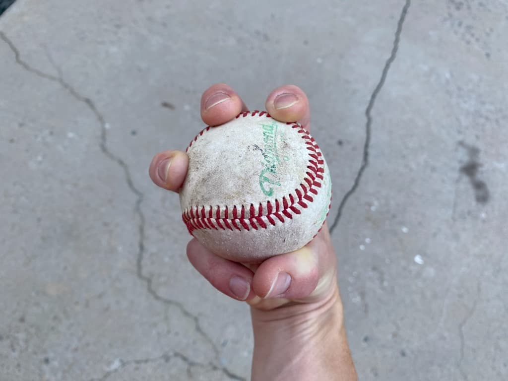Top view of a hand holding a baseball demonstrating the grip for a three-finger changeup pitch