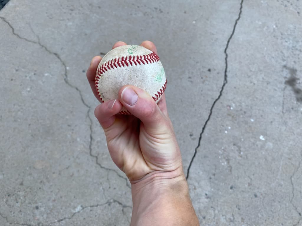 Bottom view of a hand holding a baseball demonstrating the grip for a three-finger changeup pitch