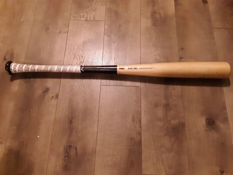 Brown baseball bat with white grip laying flat on a wood floor