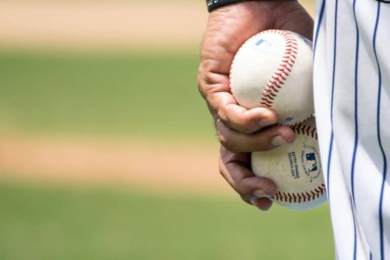 Closeup of a baseball player's hand holding two baseballs against their leg