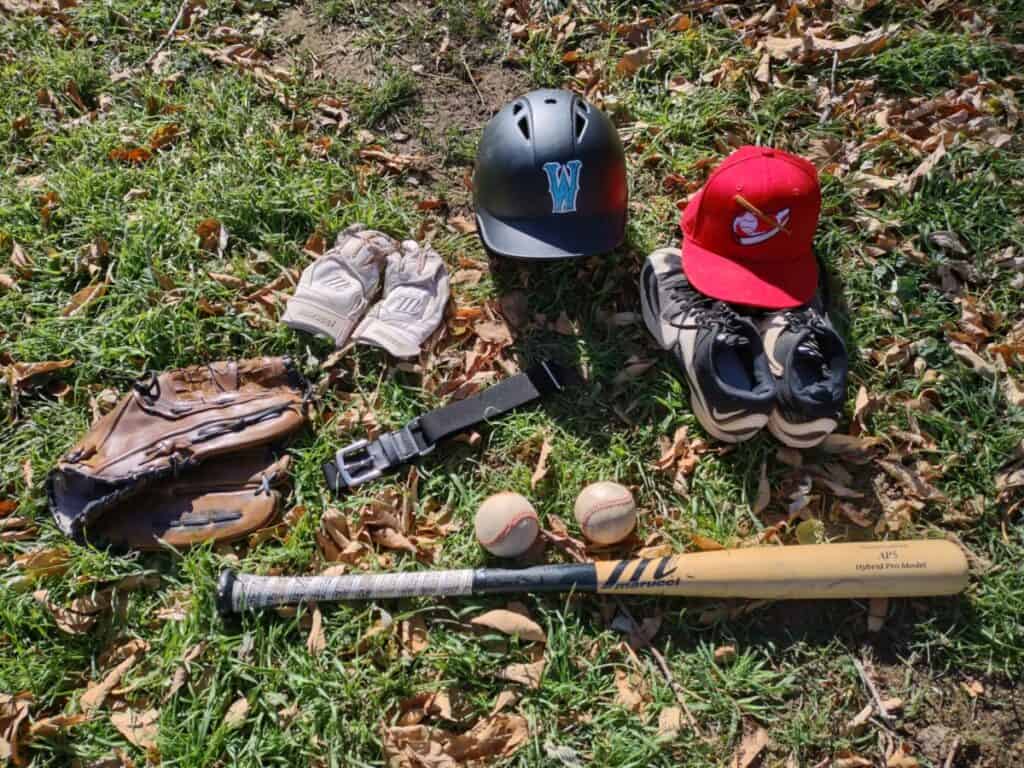 Common baseball equipment laying flat on the grass and surrounded by leaves