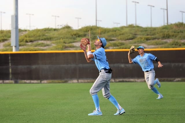 Right fielder in blue uniform waiting to catch a fly ball while teammate backs him up