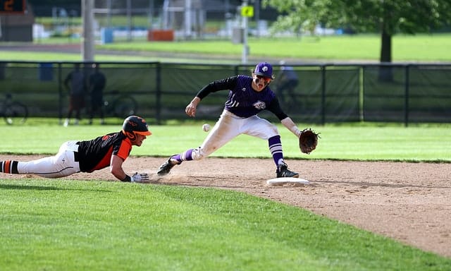 Baserunner sliding headfirst back toward second base while the shortstop is running to catch the ball