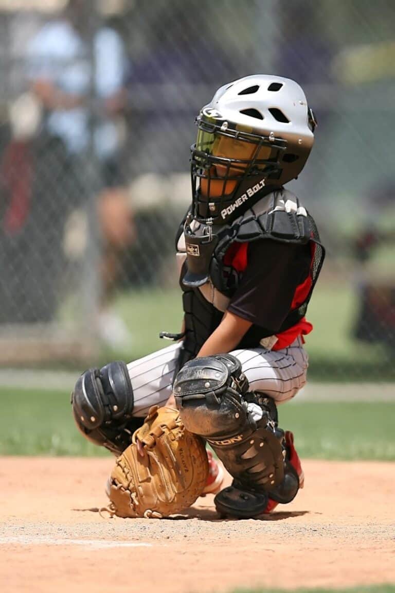 A youth baseball player in catcher's gear is signaling the next pitch