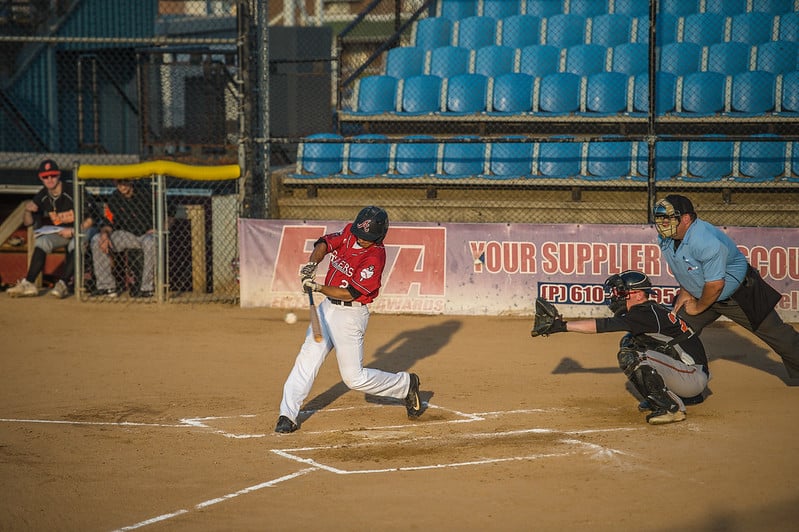 Left-handed batter wearing red uniform swings at a pitch