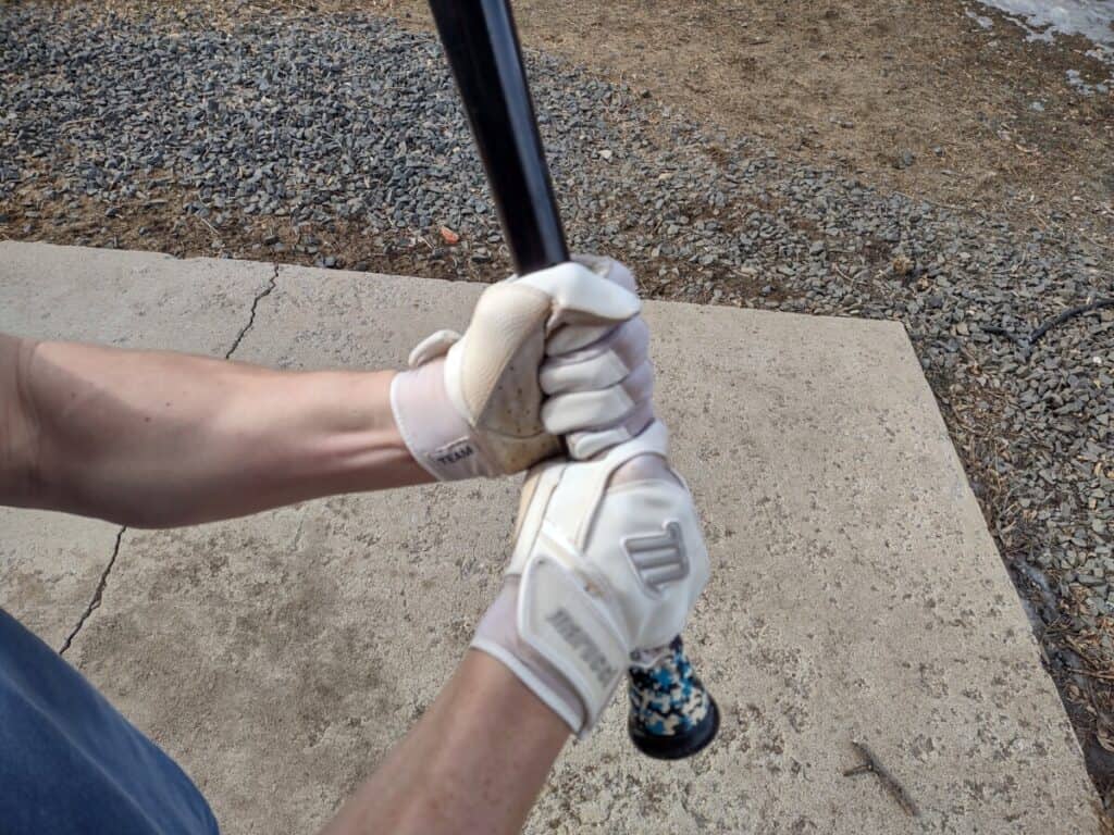 Two hands wearing white batting gloves gripping a baseball bat