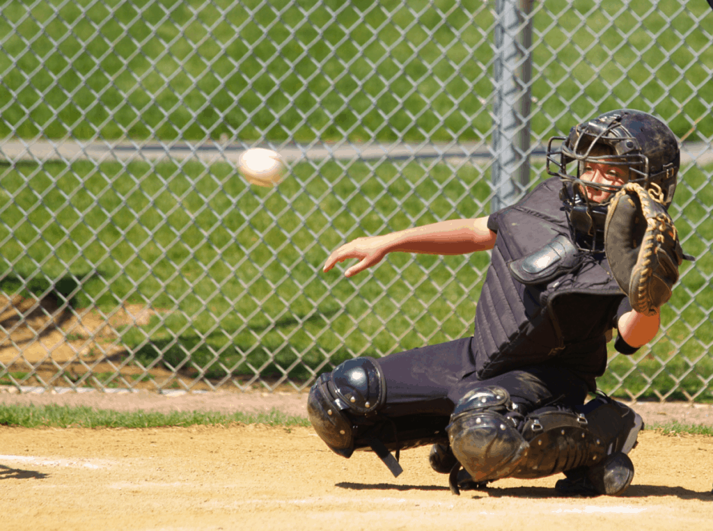 A youth catcher in all-black gear is reaching to the side to catch a pitch