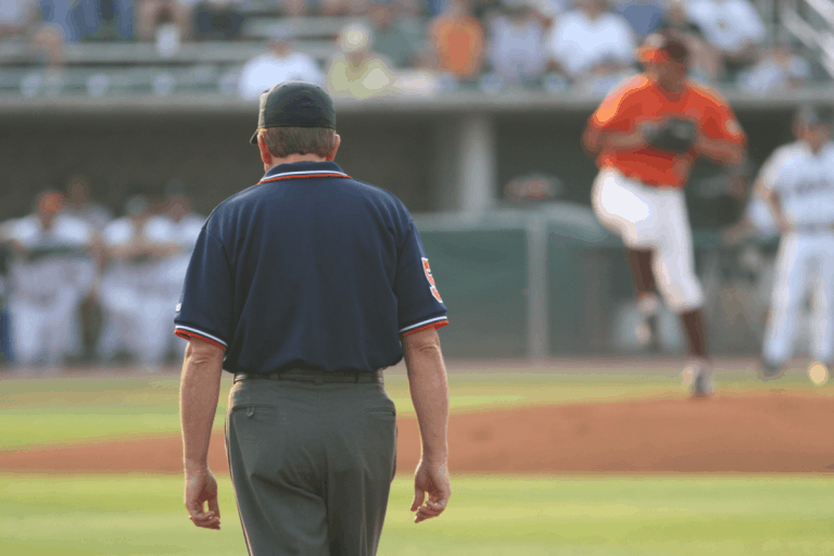 Backside view of a first base umpire watching the pitcher deliver a pitch