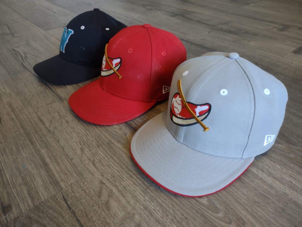 A black baseball hat, red baseball hat, and gray baseball hat laying next to each other on a wooden floor
