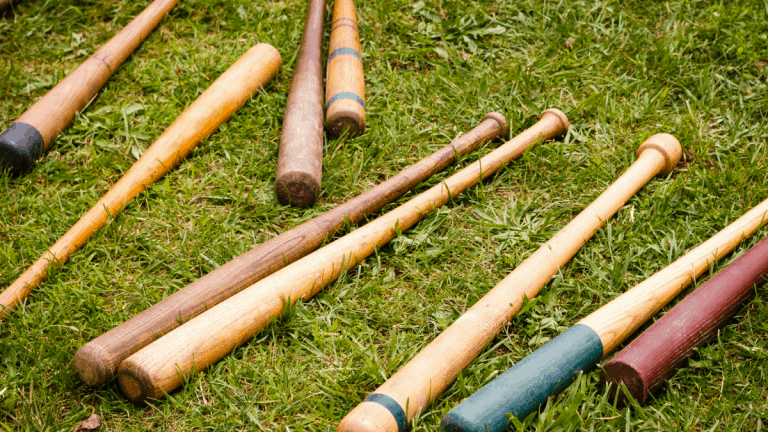 Nine wood baseball bats laying next to each other in grass