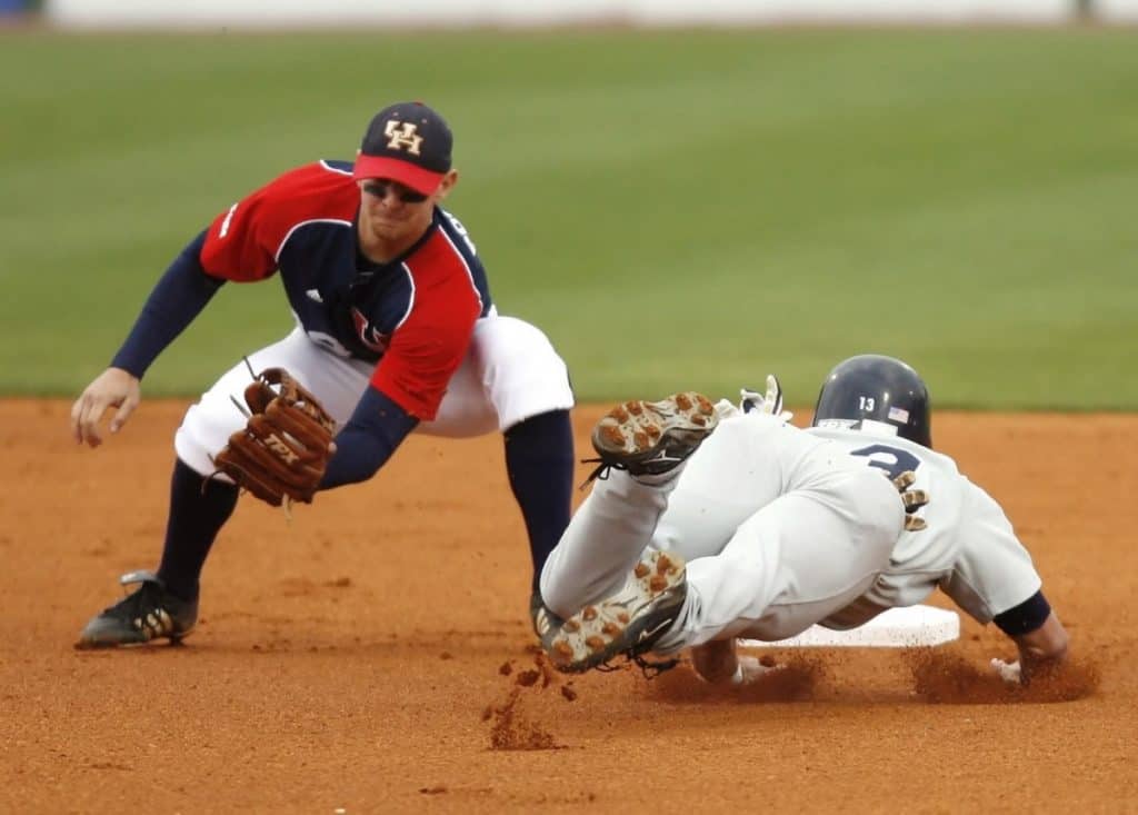 Baserunner sliding headfirst into second base while the shortstop prepares to catch a throw and apply the tag