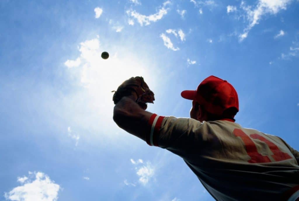 Baseball player shielding the sun with his glove so he can catch the fly ball