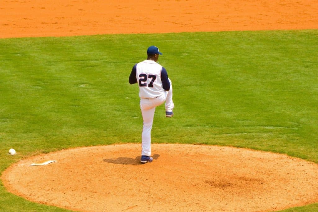 Left-handed baseball pitcher on the pitcher's mound in the middle of his windup while looking toward first base
