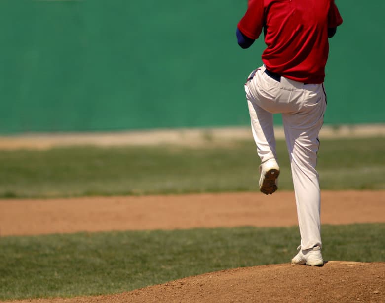 Shoulders-down view of a pitcher in a red jersey lifting his leg to deliver a pitch