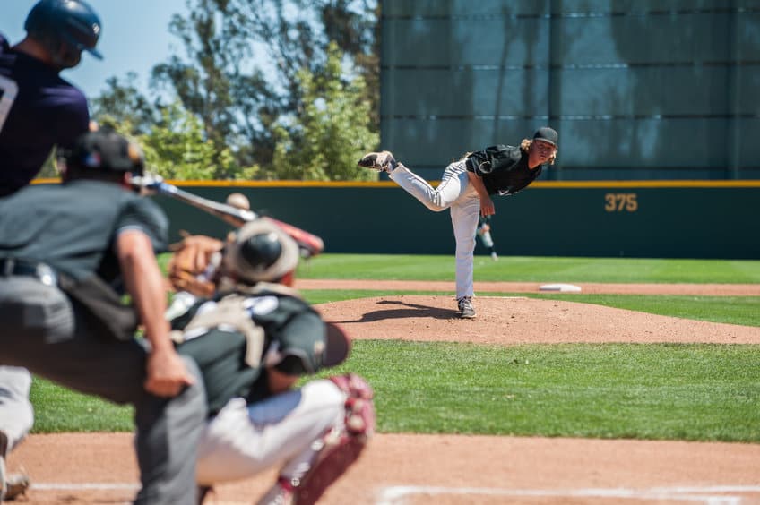 Baseball pitcher finishing his pitch while watching a right-handed batter make contact with the pitch
