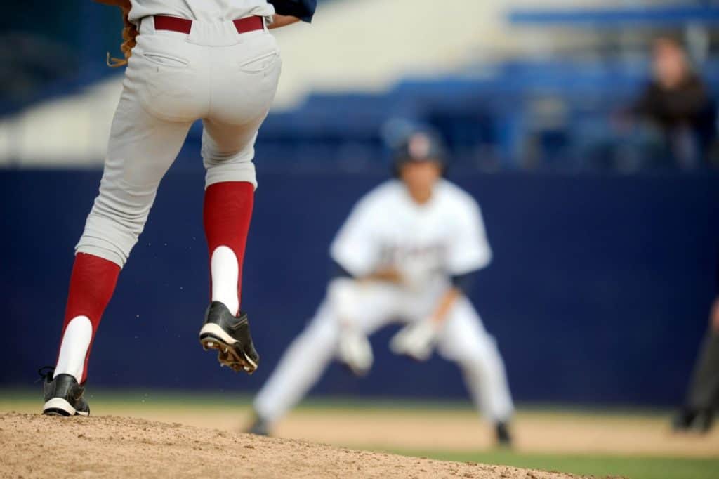 Waist-down view of a pitcher on the mound lifting his leg while wearing red stirrups