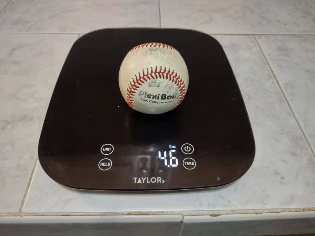 A used low compression baseball being weighed on a kitchen scale in ounces