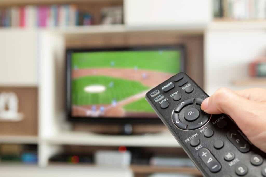 Blurry baseball game on TV with a hand holding a remote to control the TV