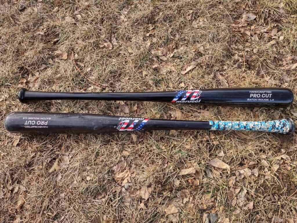 A new and a used Marucci USA Professional Cut wood bat laying parallel to each other on the grass