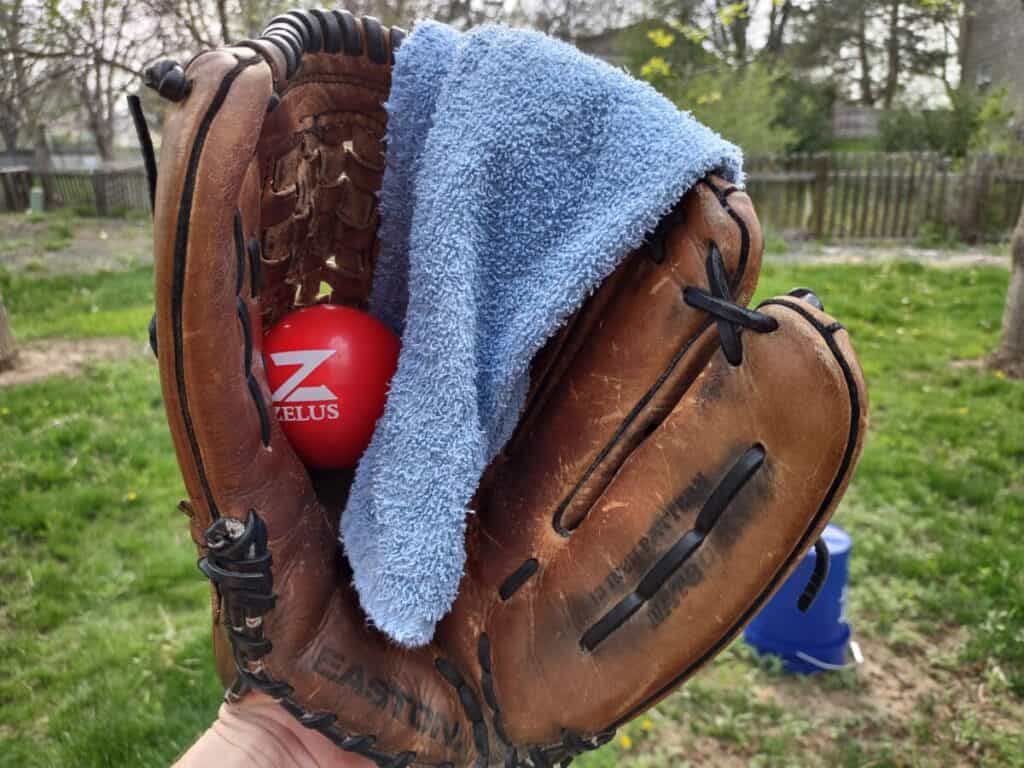 A weighted baseball inside a ball glove with a gym towel draped over the glove