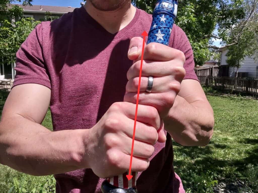 Demonstrating how to use the over grip batting grip when holding a baseball bat. A red line is going through the hands to show how one set of knuckles overlaps with the knuckles on the other hand.
