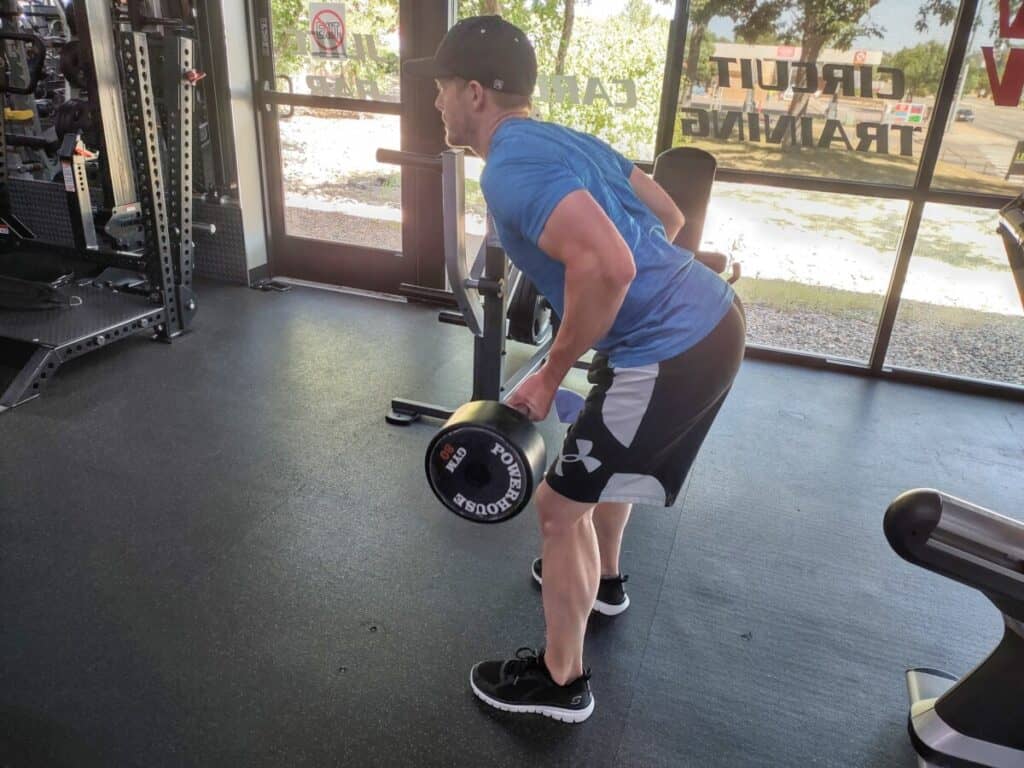 Demonstrating how to perform the bent over low row exercise with a straight bar. Player is raising the straight bar to just below his belly button.