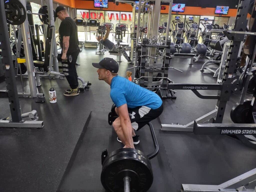 Starting position for a deadlift exercise. Player is bent down with a straight back and gripping the hex bar with both hands.