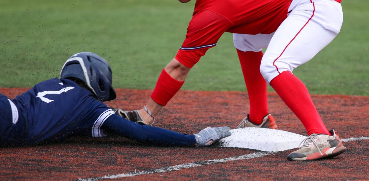 Baserunning in blue jersey sliding headfirst into third base while player in red jersey applies the tag